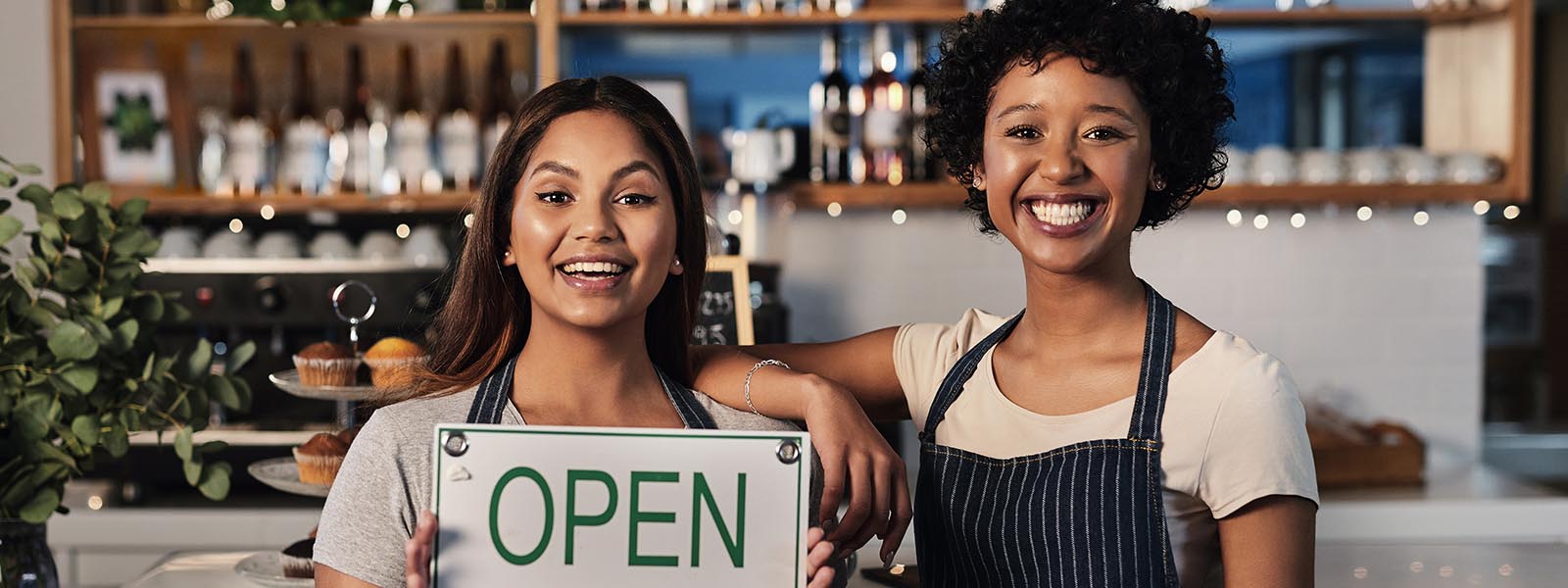 Portrait of two young women holding an open sign in a cafe.